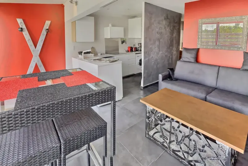 Séjour de la villa Le Donjon aux murs orangés, canapé gris et cuisine ouverte