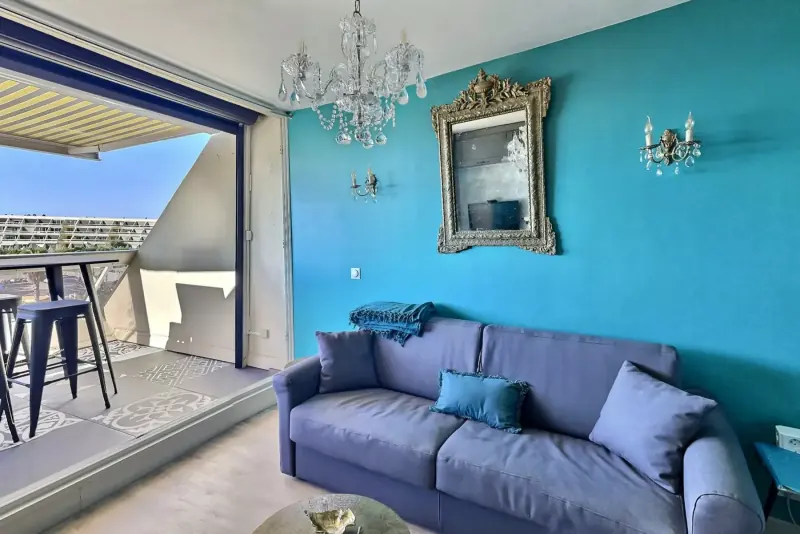 Salon turquoise avec lustre, miroir doré et terrasse ouverte sur la mer