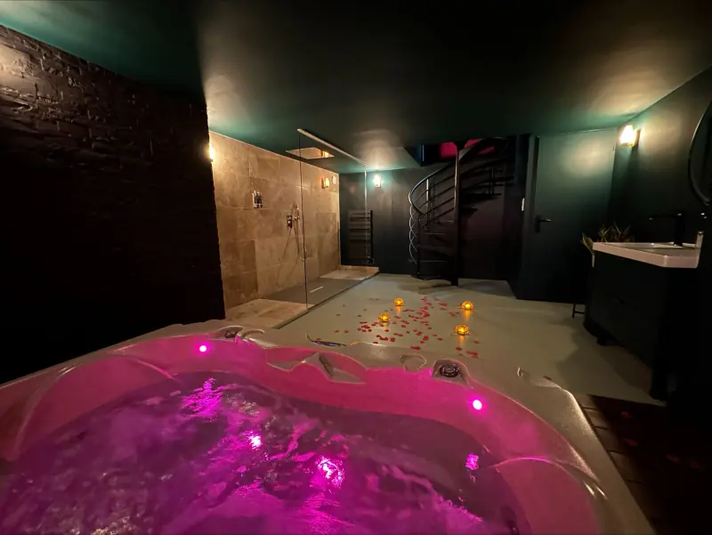 Jacuzzi privatif éclairé en rose dans la love room Velvet Désire