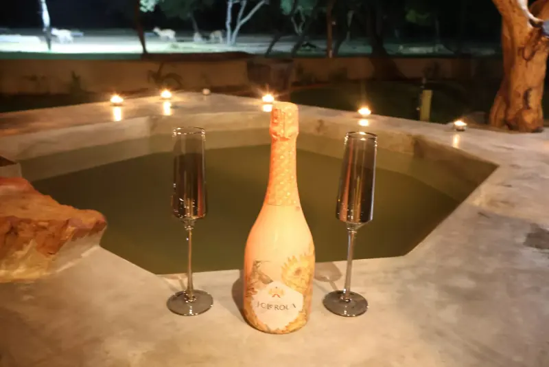 Bouteille de champagne rosé et deux flûtes au bord d'un bassin en pierre entouré de petites bougies, de nuit
