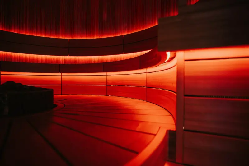 Sauna en bois aux banquettes courbes baigné d'une lumière rouge ambiante