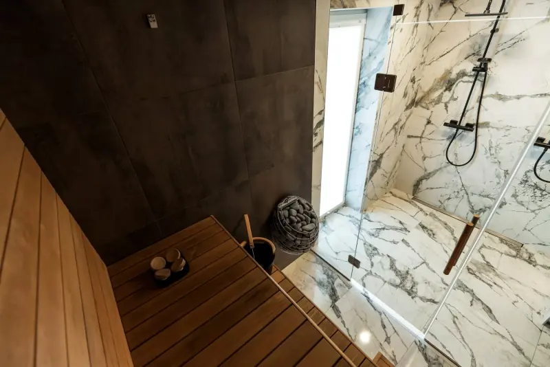 Espace bain avec un sauna en bois et une grande douche en marbre veiné derrière une paroi vitrée